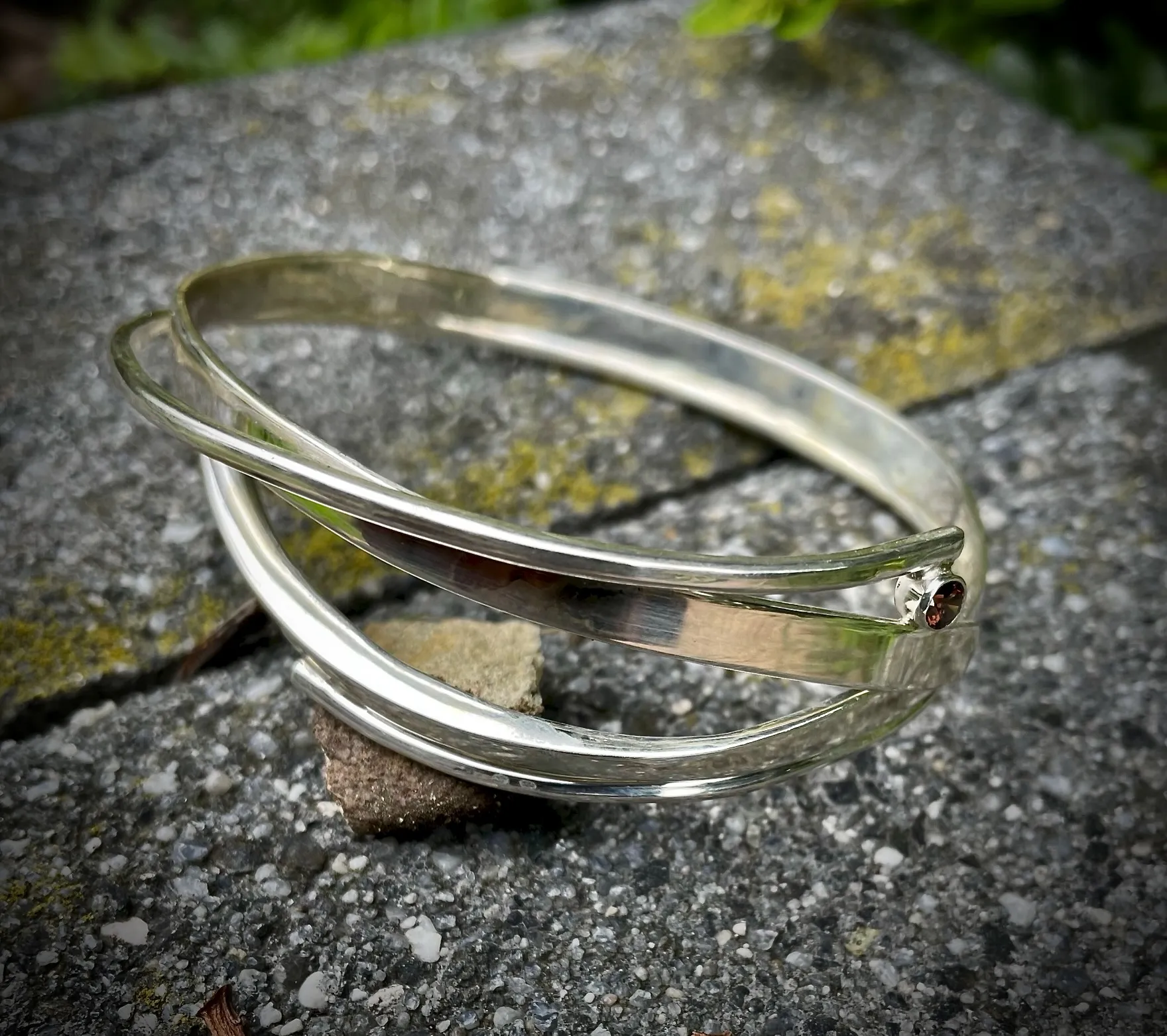 Drie overlappende zilveren bangles met kleine granaat